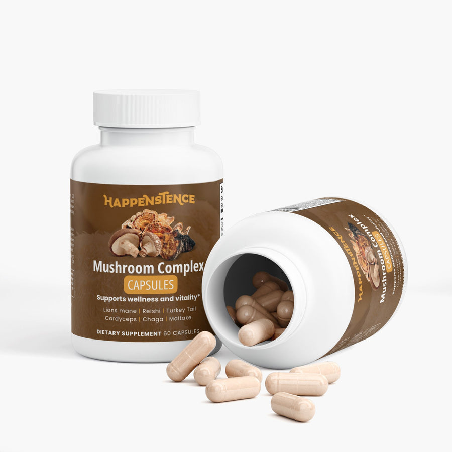 A white bottle of Happenstence Mushroom Complex dietary supplement capsules stands upright next to another tipped-over bottle showing spilled beige capsules, on a clean white background.