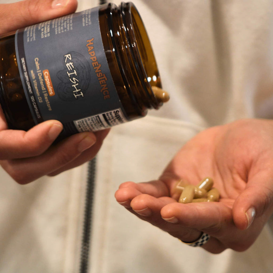 Person holding a bottle of Reishi mushrooms with pills in their hand