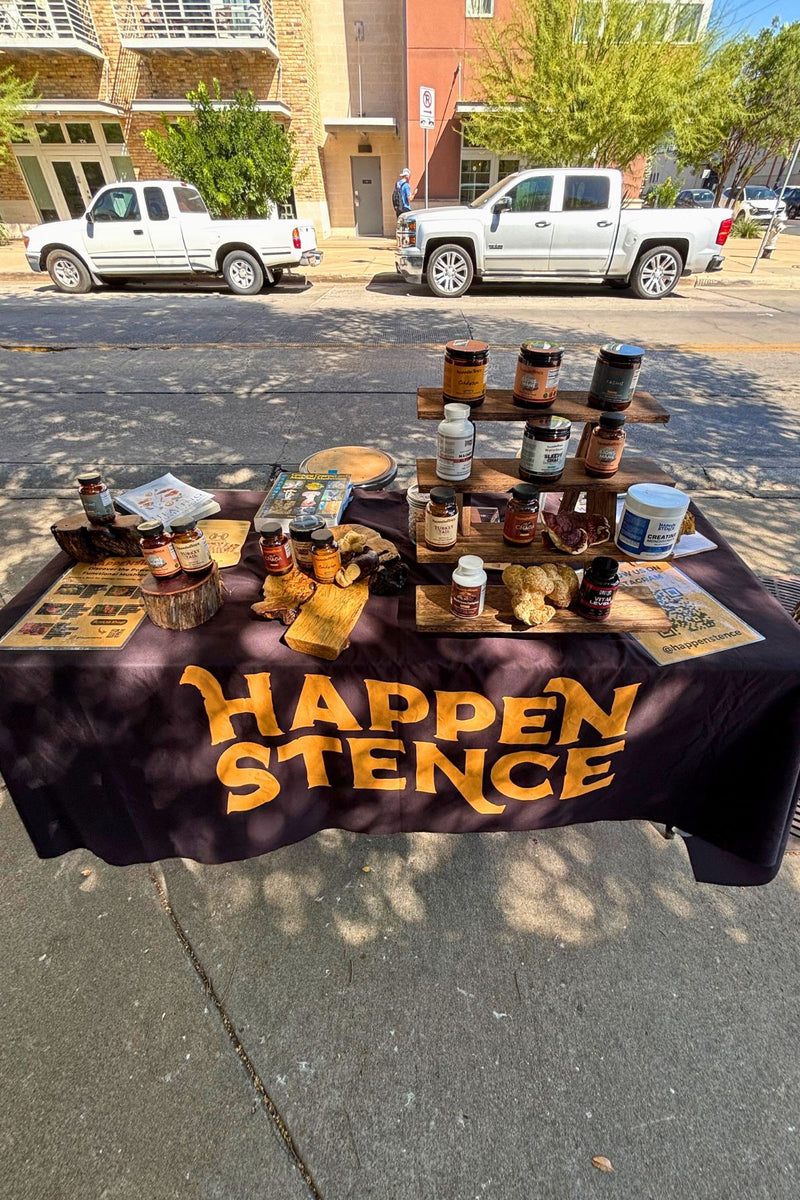 Table with various items on a street, featuring a tablecloth with 'Happen Stence' text.